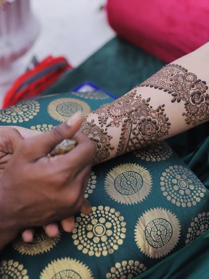 A close-up shot of a mehendi artist applying intricate henna designs on the bride's arm, highlighting the artistry and tradition.