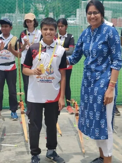 A moment of recognition for a promising young archer. She is being presented with her gold medal, a result of her focus and disciplined training at the academy.