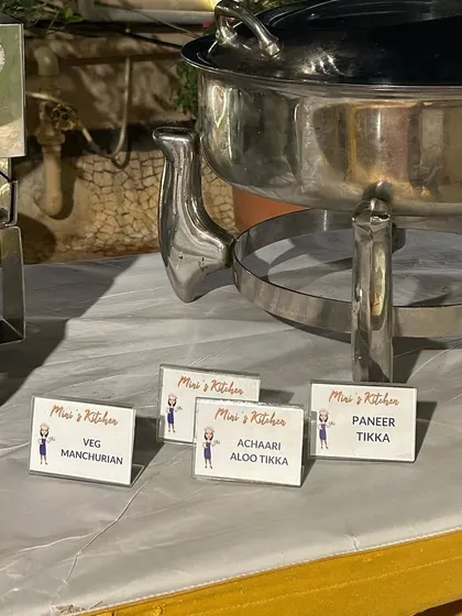 A buffet and live tandoor setup for a party in Bandra. I provide clear labels for each dish, including Veg Manchurian, Achaari Aloo Tikka, and Paneer Tikka.
