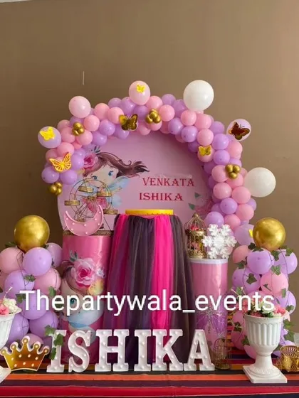 A beautiful naming ceremony decoration in pink and gold. The setup includes a custom backdrop, floral arrangements, and light-up letters for the baby's name.