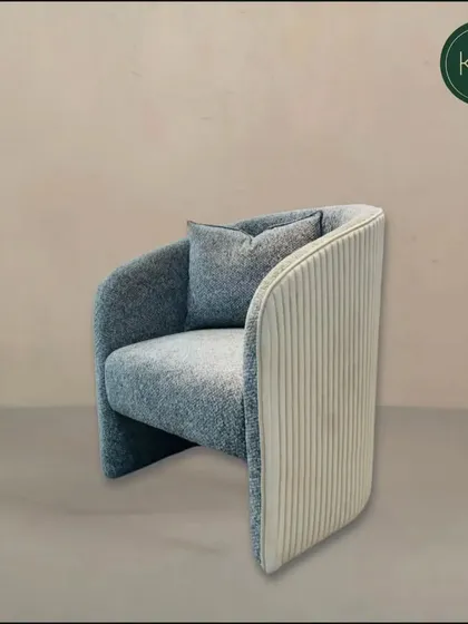 This contemporary armchair combines a textured blue fabric with a vertically ribbed back panel in a contrasting cream color. The curved design offers a comfortable and stylish seating experience.