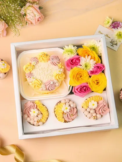 A top-down view of a Mother's Day themed bakery hamper, filled with a mini cake, cupcakes, and flowers.