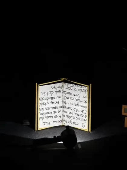 A single puppeteer kneels before a giant, illuminated book in 'Mamulengo de la Mancha'. This show creatively blends different forms of puppetry, including object and shadow theatre.