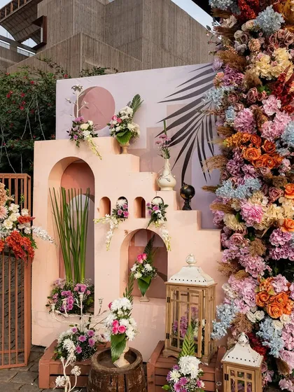 A stunning, multi-layered decor installation for a carnival-themed event, featuring pastel-colored architectural elements and a cascade of colorful flowers.