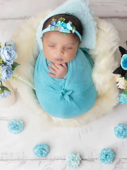 A top-down view of a sleeping newborn in a fluffy white basket, surrounded by blue flowers.