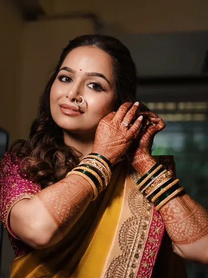 Getting ready moments. This shot highlights the intricate mehendi and traditional green and gold bangles, essential parts of the Marathi bridal ensemble.
