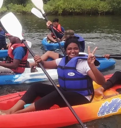 A participant flashes a peace sign from her kayak, showing the fun and friendly atmosphere of our summer camps.