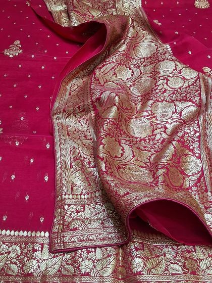 A classic red Banarasi saree, laid out to show its magnificent zari work on the border and pallu. This piece is a must have for any bridal trousseau or major festive event, offering a look of pure opulence.