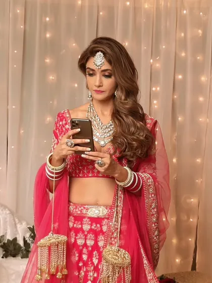 Full Hollywood glam for this bride. The look features voluminous side-swept waves, a smokey eye, and a vibrant pink lehenga, creating a stunning and memorable style for any wedding event.