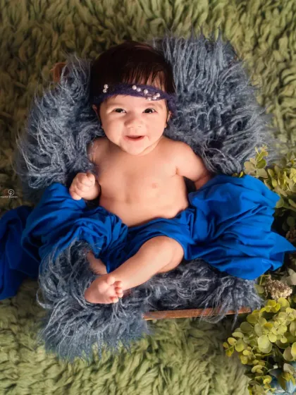 A beautiful color combination of royal blue and green makes this baby portrait pop. The baby is propped up in a basket, looking off to the side with a curious expression.
