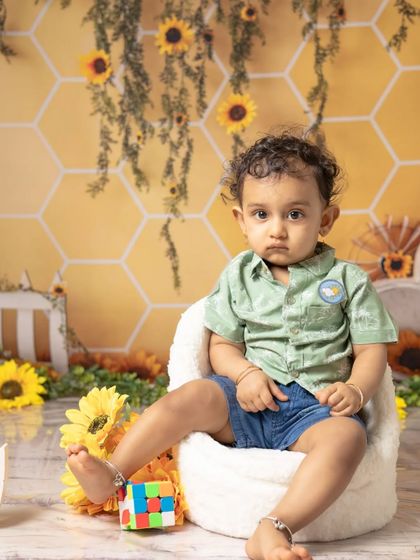 This little boy looks thoughtful before diving into his sunflower-themed cake smash. The yellow and green setup creates a bright and cheerful atmosphere.