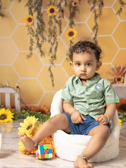 This little boy looks thoughtful before diving into his sunflower-themed cake smash. The yellow and green setup creates a bright and cheerful atmosphere.