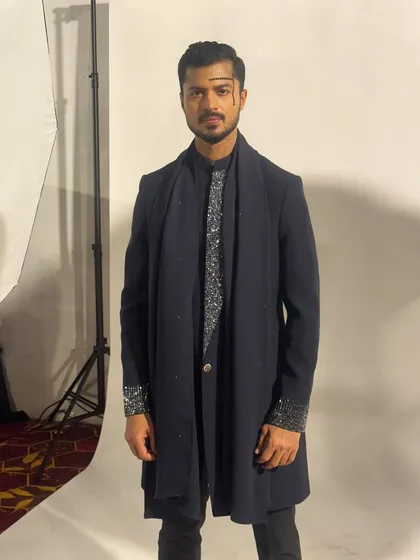 A studio-style shot taken backstage, showing the sharp silhouette of the designer's creation against a white background.