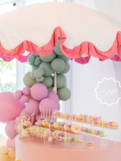 The stunning dessert cart at "Aahana's Onderland," sheltered by a scalloped umbrella and decorated with a pastel balloon cascade.