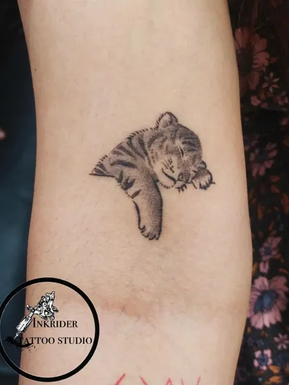 A tiny, sleeping tiger cub. This adorable tattoo uses fine lines and soft shading to capture a moment of peace and innocence.