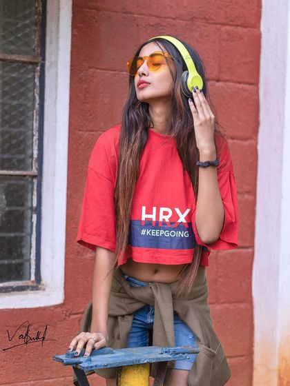 Capturing a cool, music-loving vibe on the street. The combination of the headphones, sunglasses, and casual HRX crop top creates a portrait that is full of personality and modern athletic style.