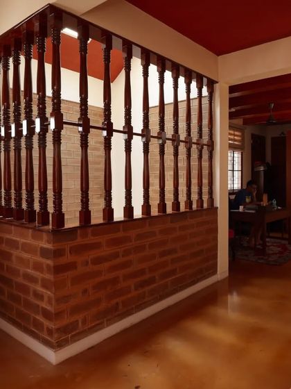 A wooden balustrade separates spaces while maintaining visual connection, set against an exposed brick wall and warm yellow oxide flooring.