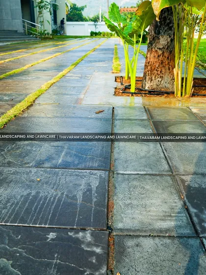 This modern driveway design incorporates strips of grass between large, dark stone tiles, breaking up the hard surface and adding a touch of green.