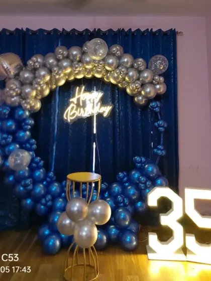 A 35th birthday home setup with a blue and silver balloon ring, marquee numbers, and a curtain backdrop.