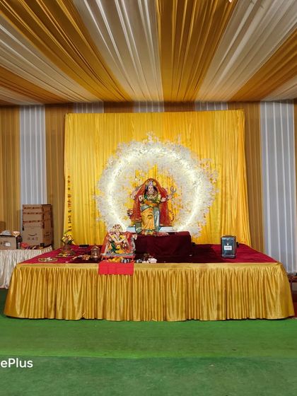 A stage for the Devi idol during Navratri. The backdrop is made of bright yellow drapes with a ring of white flowers, creating a divine focal point.