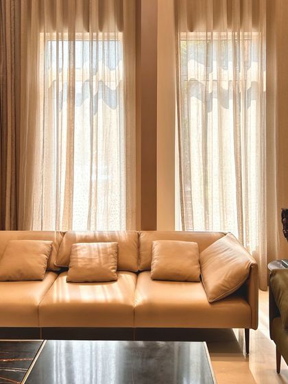 The interplay of light and shadow through the sheer curtains adds a soft, dynamic quality to the living space. The choice of neutral-toned furniture creates a calm and serene atmosphere.