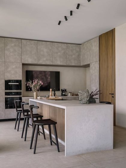 The kitchen is designed to be both functional and beautiful, with a large central island and handleless cabinetry. The mix of concrete-finish surfaces and warm wood creates a modern, sophisticated look.