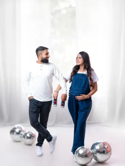 A fun, casual shot with disco balls. The couple, holding tiny baby shoes, looks happy and relaxed, ready for the next big adventure.