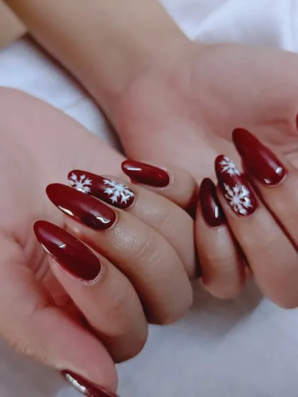A festive winter set with a deep red polish and hand-painted white snowflakes.