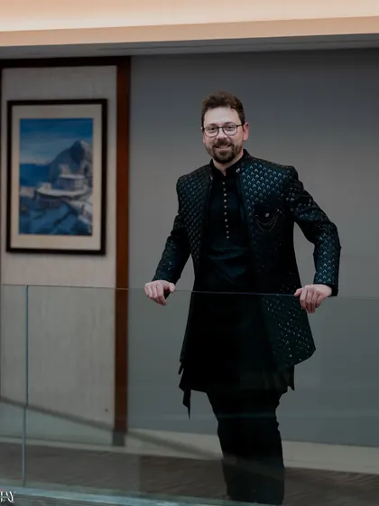 A confident and stylish portrait of the groom. He leans against a glass railing, and the clean lines of the modern interior create a sharp and sophisticated look.