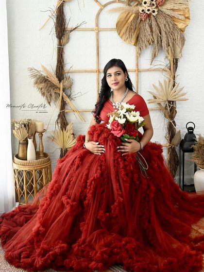 A serene moment in the boho setup. Seated amongst natural textures and holding a bouquet, the mom-to-be looks peaceful and radiant in her red gown.