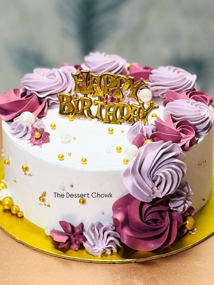 A lovely birthday cake with purple and pink buttercream rosettes. The gold "Happy Birthday" topper and sprinkles add a festive touch.