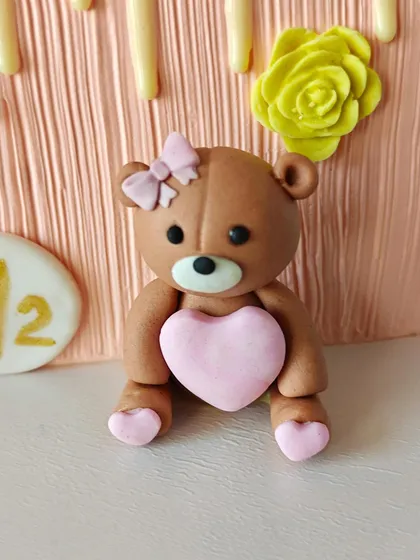 A close-up of the adorable, handcrafted fondant teddy bear from the half-birthday cake, complete with a tiny bow and a heart.