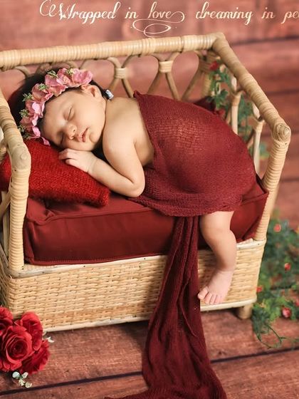 Another angle of the red-themed newborn session. The long, flowing wrap adds a sense of drama and elegance to the portrait, while the baby remains peacefully asleep in the rattan bed.