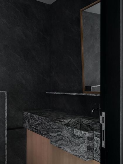 A bathroom vanity I designed in darker tones. The sink is carved from a piece of heavily figured granite, and the cabinet below is a simple wood veneer, letting the dramatic stone be the star.