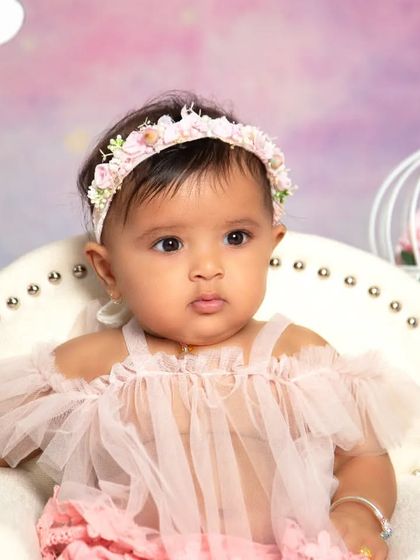 A regal portrait from a unicorn-themed half-birthday shoot. The baby sits confidently in a mini throne chair, surrounded by whimsical props like a birdcage and teepee.