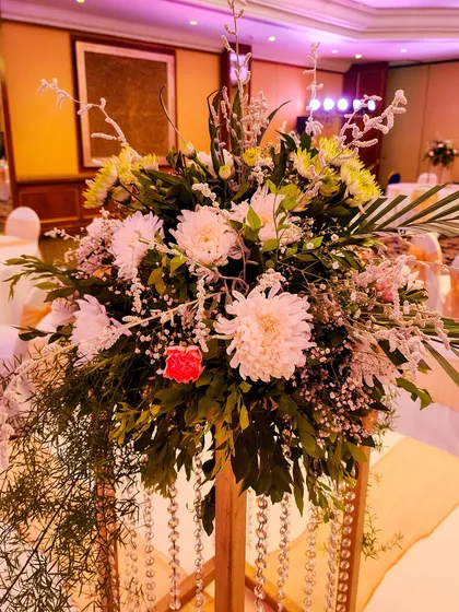 A tall floral arrangement on a wooden stand, featuring white chrysanthemums and cascading crystal strings. This type of elevated centerpiece adds height and drama to the room.
