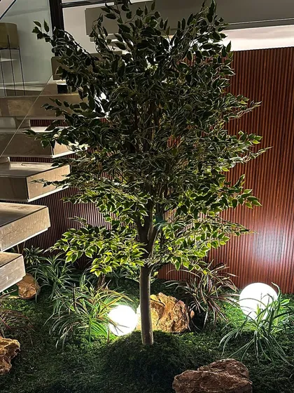 A full, leafy artificial tree stands as the centerpiece of this mossy under-stair garden. The spherical lights scattered throughout the moss bed create a whimsical, enchanted forest feel after dark.