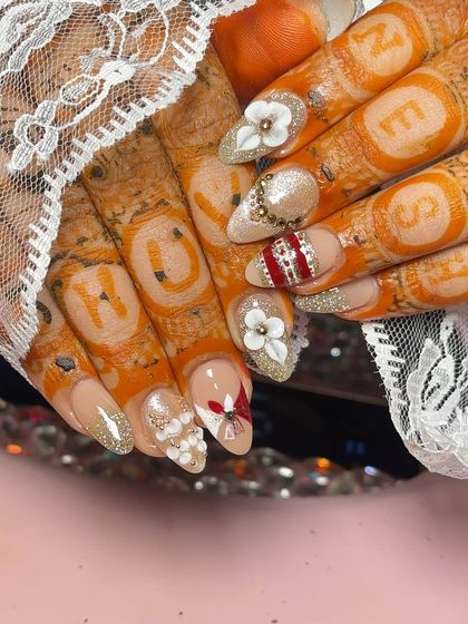 It's all in the details. This personalized bridal set includes the groom's initials hidden in the mehendi, complemented by nails with 3D flowers, glitter, and a traditional red and white 'choora' inspired design.