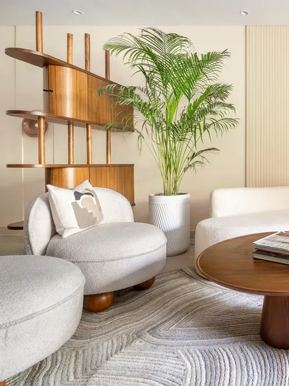 A sculptural wooden partition subtly divides the space, adding an artistic element while maintaining the open and airy feel. A large plant brings a touch of nature indoors, enhancing the room's tranquil vibe.
