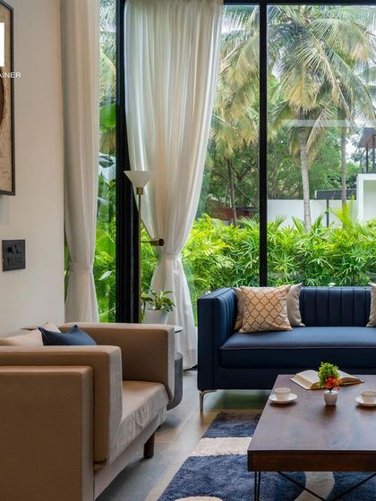 The living room of this villa is designed for comfort and style. The combination of a classic blue sofa and a neutral armchair, paired with large windows, creates a bright and inviting space for relaxation.