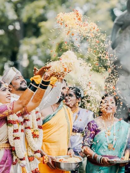 Another angle of the Akshata ritual, showing the bride and groom joyfully showering each other with rice and flowers, surrounded by their loved ones.