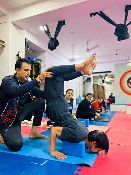 I am providing support to a student as he works on his Scorpion Pose using a block. This hands-on guidance ensures he maintains proper form and avoids injury.