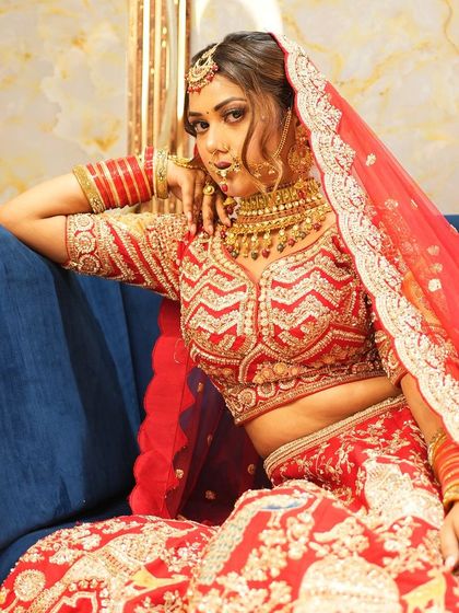 A bride seated in a regal pose, showcasing the rich fabric and detailed work of her red lehenga. This is the kind of outfit that makes for unforgettable wedding portraits.