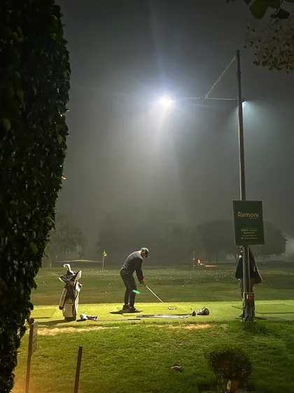 A lone golfer practices under the lights on a foggy night, creating a dramatic and focused scene.
