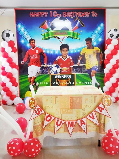 A football-themed 10th birthday party with a stadium backdrop featuring famous players. The decor is completed with red and white balloon pillars and trophy cutouts.