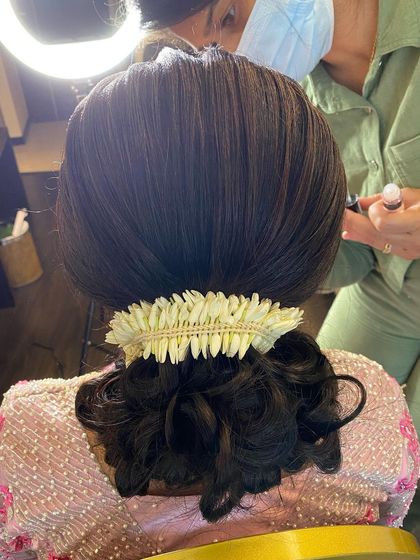 A close-up of a sleek low bun, neatly wrapped and adorned with a simple jasmine gajra.