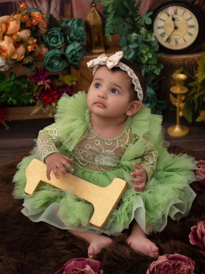 A vintage-inspired portrait. The soft green dress and rustic background create a timeless and elegant look for this 11-month milestone.