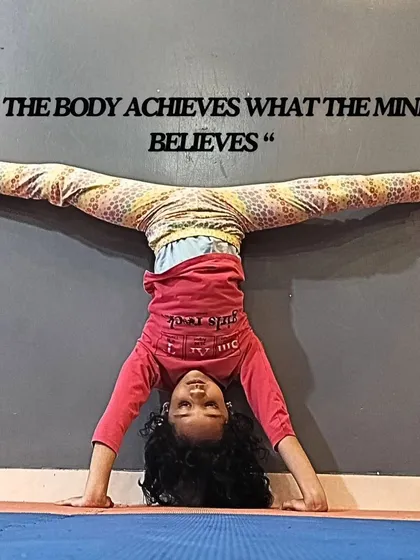 The body achieves what the mind believes. A young gymnast demonstrates incredible flexibility and strength in this wall-assisted headstand split.