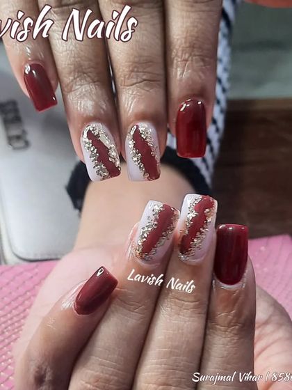 A rich maroon set with accent nails featuring a bold slash of gold glitter.