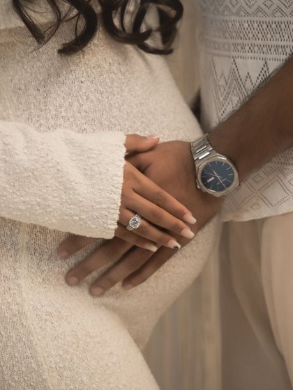 A promise of forever. This close-up shot of the couple's hands intertwined over the baby bump, showcasing the engagement ring, symbolizes the journey they are on together.